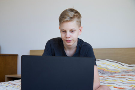 Child using gadgets to study. Homework at home. Laptop on the bed. Homeschooling during quarantine.の写真素材