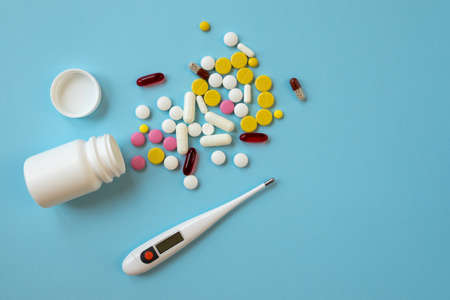 Multi-colored tablets, pills, capsules and digital thermometer on a blue background. Concept of treatment for a sick person. Top viewの写真素材