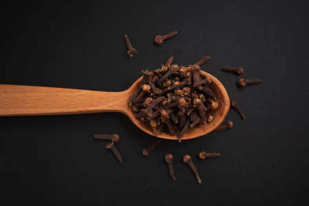 Dried cloves in a wooden spoon isolated on a black background top view.の写真素材