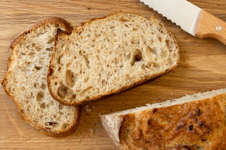 Fresh bread slice and cutting knife on chopping board. Food close up.