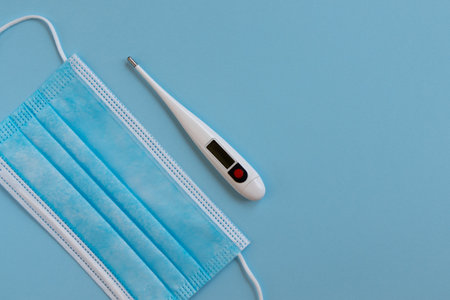 Medical surgical mask. Face mask and digital thermometer on blue background. Flu  virus protection....