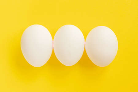 White chicken eggs on yellow background. Top view. Healthy food concept.の写真素材