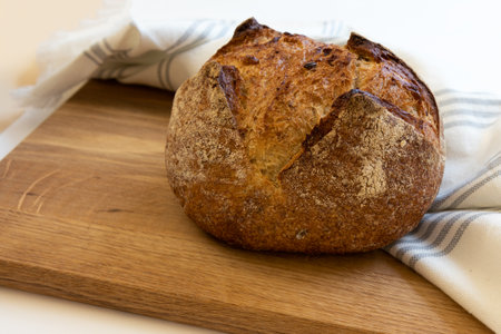 Freshly baked homemade bread wrapped in white linen towel lying on a wooden table