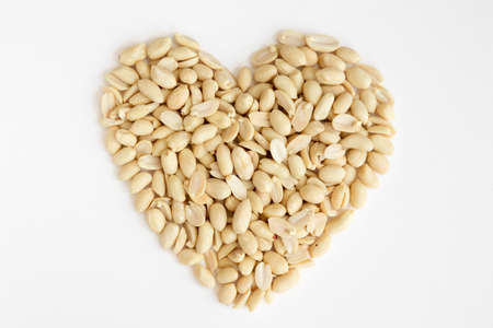 Salted peeled peanuts in a heart shape isolated on white background. Flat lay. From above.