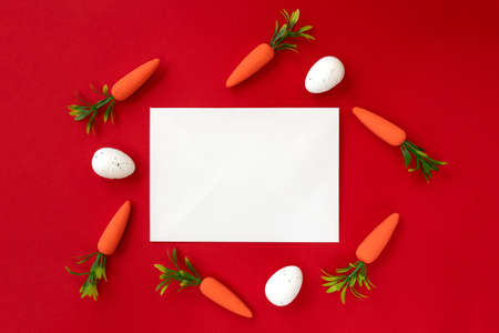 Creative layout made of Easter eggs and carrots with blank paper card on a red background. Minimal...
