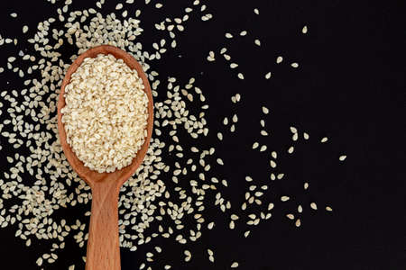 White sesame seeds in wooden spoon on pile of white sesame seeds, top view.の写真素材