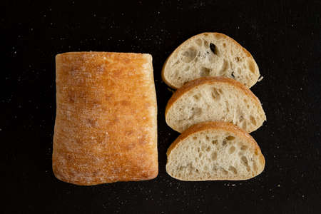 Sliced ciabatta bread on black rustic background. Sliced Italian Ñhiabata. Top view