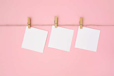 Empty paper sheet for notes, frames that hang on rope with clothespin and isolated on pink background. White blank with empty space for text.の写真素材