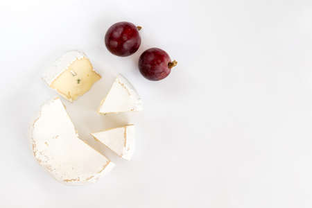 Pieces of camembert or brie cheese with red grapes isolated on white background. Soft cheese covered with edible white mold view from above. Gourmet blue cheese.の写真素材