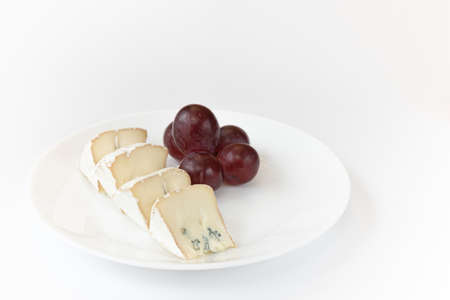 pieces of camembert or brie cheese with red grapes on plate isolated on white background, soft...