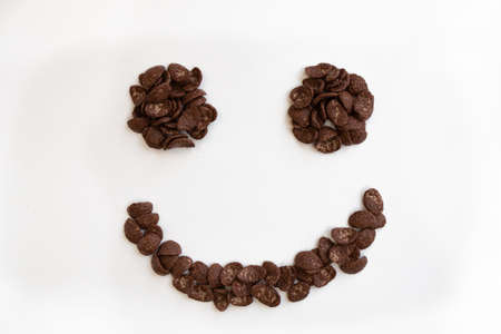cereal muesli breakfast in the shape of smiling face on white background, healthy eating, food and lifestyle concept, chocolate corn flakes, top view, close upの写真素材