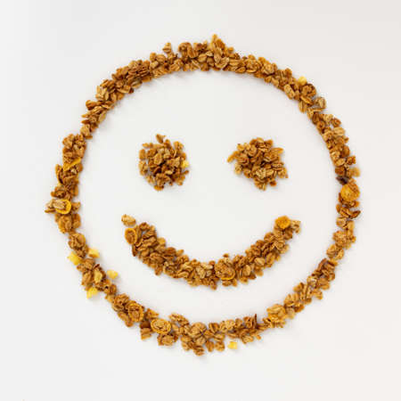 crunchy granola breakfast in the shape of smiling face on white background, healthy eating, food and lifestyle concept, cereal flakes, top view, close upの写真素材