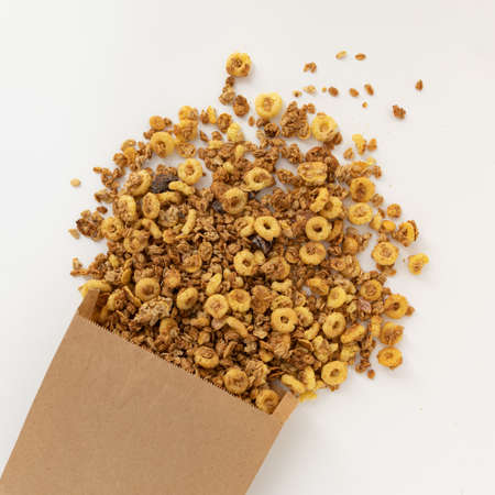 crunchy granola for breakfast, tasty granola poured out of paper bag isolated on white background,...