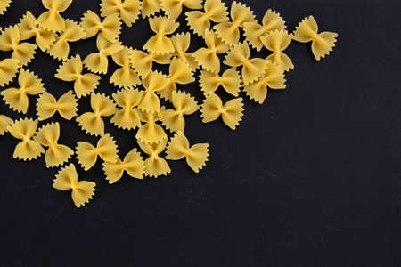 raw pasta farfalle with empty space for text on black background, top view of italian cuisine ingredientの写真素材