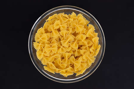 pasta farfalle in glass bowl isolated on black background, raw pasta in shape of bow, top viewの写真素材