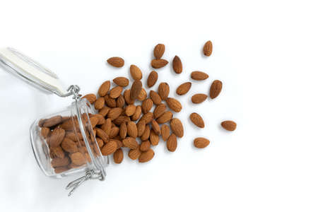 peeled almonds nuts poured out of glass jar on white background, concept healthy food, top viewの写真素材