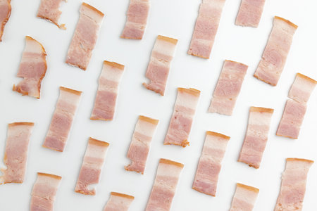 pieces of bacon as pattern on white background, minimal food concept, close up of fresh or uncooked thin sliced baconの写真素材