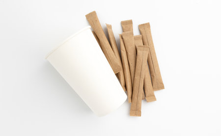 sugar sticks and paper cup, sugar in paper kraft packaging, mock up for design isolated on white backgroundの写真素材
