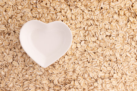ceramic bowl as heart shape on background of oatmeal, instant cereal, healthy breakfast conceptの写真素材