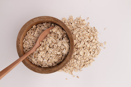 dry rolled oatmeal in wooden bowl with spoon isolated on white background, health breakfastの写真素材