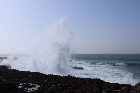 Big waves breaking on the shore rocks with sea foam.