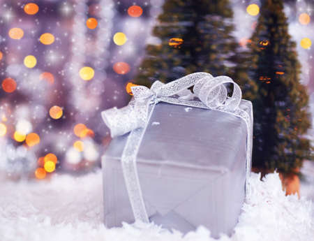 Winter holiday background with present gift box, silver ribbon ornament & Christmas snow decoration & defocus lightsの写真素材