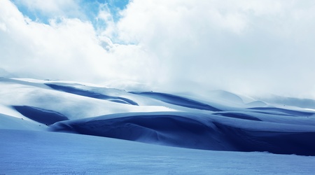 Winter landscape of high mountains with snow blizzard and fresh blue sky, beautiful nature panoramic backgroundの写真素材