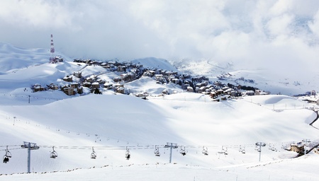 Winter mountain ski resort landscape with snow and cute little houses, chairlift with people playing sportの写真素材