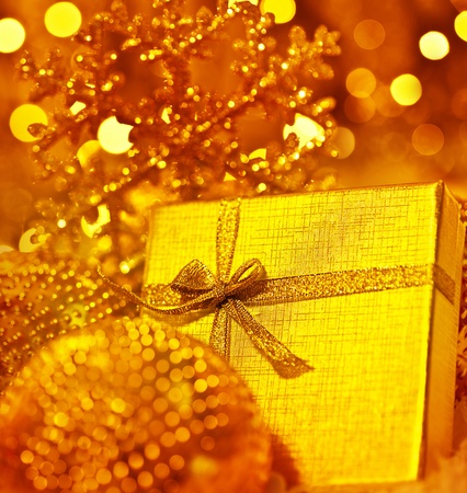 Golden gift box with baubles decorations, Christmas tree ornament for winter holidays, present with abstract bokeh shiny glowing blur lights backgroundの写真素材