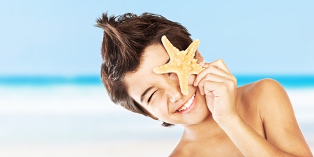 Happy face cute boy with starfish on the beach, closeup portrait of preteen brunette child, male kid model having fun outdoor, summer travel and beach vacationの写真素材