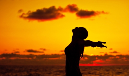 Woman silhouette over sunset sky, dark black shadow of female body with hands up, teenage girl having fun outdoor, enjoying sundown on the beach, freedom lifestyle, happiness concept の写真素材