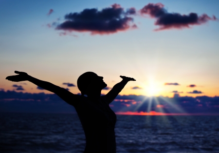 Woman silhouette over sunset sky, dark black shadow of female body with hands up, teenage girl having fun outdoor, enjoying sundown on the beach, freedom lifestyle, happiness conceptの写真素材