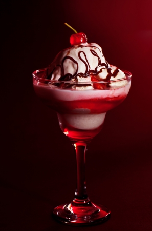 Cold fruity ice cream, tasty vanilla frozen yogurt still life isolated on red background, cherry jam and liquid chocolate topping, sundae in the glass, sweet food styling, decorated design dessertの写真素材