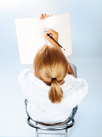 Student girl passing exams in classroom, cute schoolgirl drawing in textbook, sweet teenager writing letter on blank paper, young female sitting on chair rear view, education concept, back to schoolの写真素材