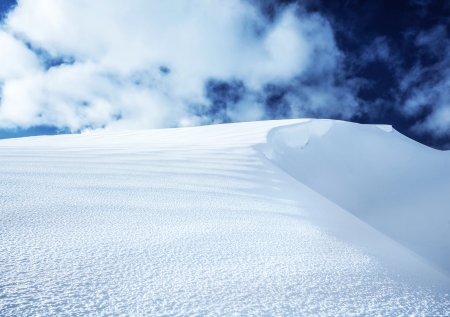 Image of beautiful snowy hill and dark blue cloudy sky, top of the mountain covered with white snow, peaceful winter landscape, wintertime seasonal weather, Christmastime vacationの写真素材