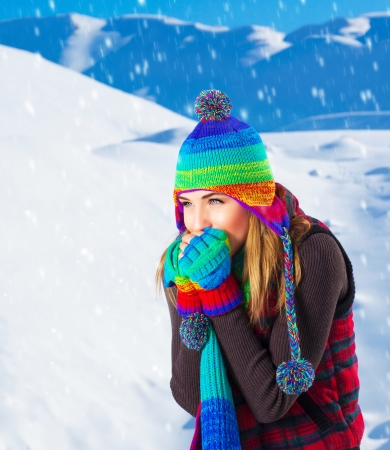 Picture of cute female in winter mountains, snowfall outdoors, beautiful woman wearing colorful wool hat, scarf and gloves, woman froze outdoor in cold snowy weather, wintertime holidaysの写真素材