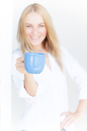 Blur image of cute blond girl hold blue cup of coffee on white background, morning drink, happiness conceptの写真素材