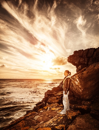 Traveler girl on the cliff, beautiful sunset on seascape, photographer woman, active lifestyle, expedition to mountains, travel conceptの写真素材