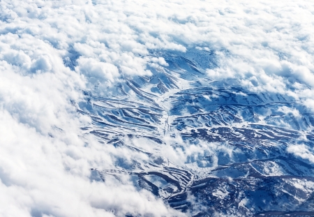 Bird's eye view on snowy mountains, scene on the mountain through white fluffy clouds, winter holidays, cold weather
の写真素材