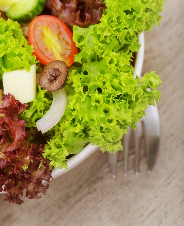 Closeup on traditional greek salad in the plate on wooden table served with fork, green lettuce, fresh vegetables, delicious cuisine, healthy eating conceptの写真素材
