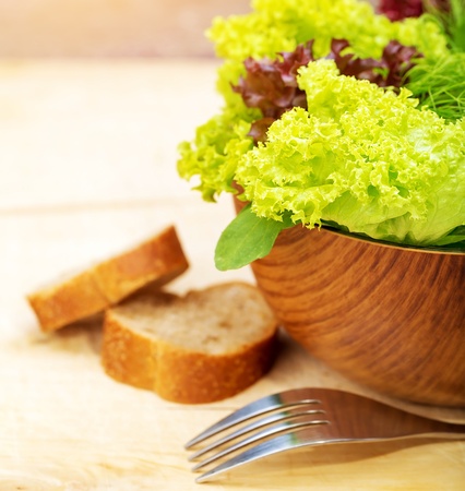Lettuce salad with two slice of bread on wooden table, shiny fork, fresh green vegetables, organic food, healthy nutrition, dieting conceptの写真素材