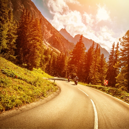 Motorcyclists on the mountainous road in bright red sunset light, riding on highway pass along Alpine mountains, enjoying extreme sport, travel and tourismの写真素材