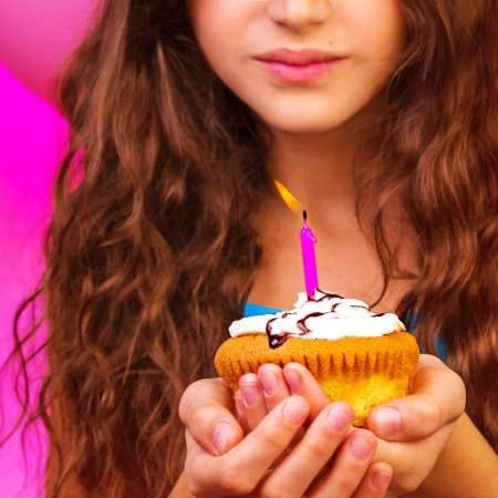 Lovely birthday girl make a wish with sweet festive cupcake in hands, enjoying holiday celebration, having fun indoors, happiness conceptの写真素材
