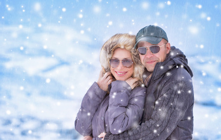 Closeup portrait of beautiful couple standing under snowfall in the mountains, romantic wintertime vacation, cold weather, love conceptの写真素材