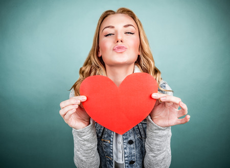 Portrait of cute teen girl with red paper heart isolated on gray background, kiss with love, Valentine day, affection conceptの写真素材