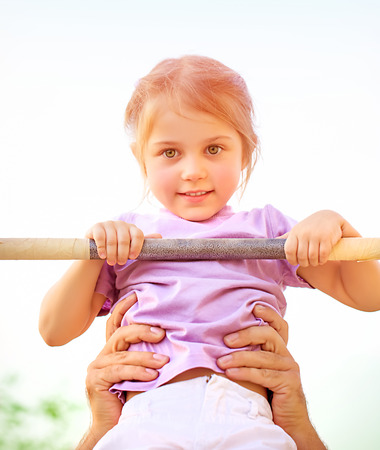 Portrait of cute little girl lifting on horisontal bar outdoors, sportive activities in daycare,...
