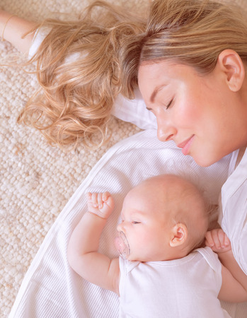 Portrait of sweet newborn child with young mom sleeping on the bed at home, time of day dreaming, healthy lifestyle conceptの写真素材
