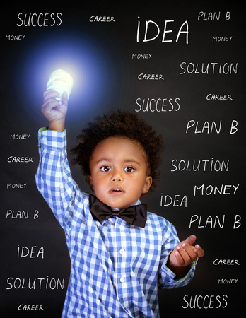 Portrait of little African genius boy with lightbulb in the hand on blackboard background, back to school, find solution conceptの写真素材