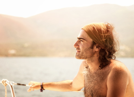 Portrait of man sitting on sail boat and enjoying mild sunset light, handsome captain of luxury water transport, summer vacation conceptの写真素材