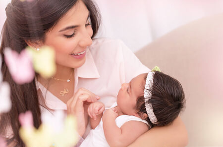 Portrait of beautiful young female holding on hands cute newborn daughter, enjoying motherhood, soft...